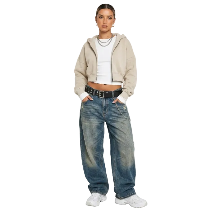Model wearing a light beige cropped zip hoodie and baggy vintage wash denim jeans with a black belt for a Y2K streetwear look.