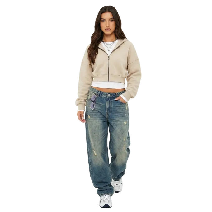Model posing in a beige cropped zip hoodie and baggy vintage wash denim jeans for a Y2K streetwear look.