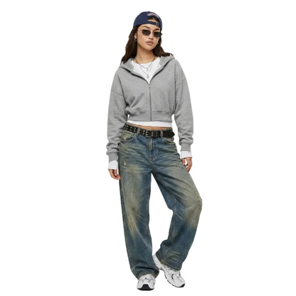 Model posing in a grey cropped zip hoodie, baggy vintage wash denim jeans, and a backward cap for a Y2K streetwear look.