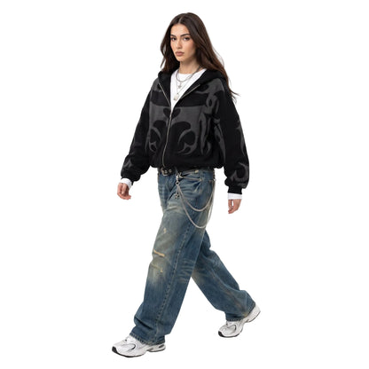 A model wearing a black graphic zip-up hoodie and baggy vintage wash denim jeans with a chain belt for a Y2K streetwear look.